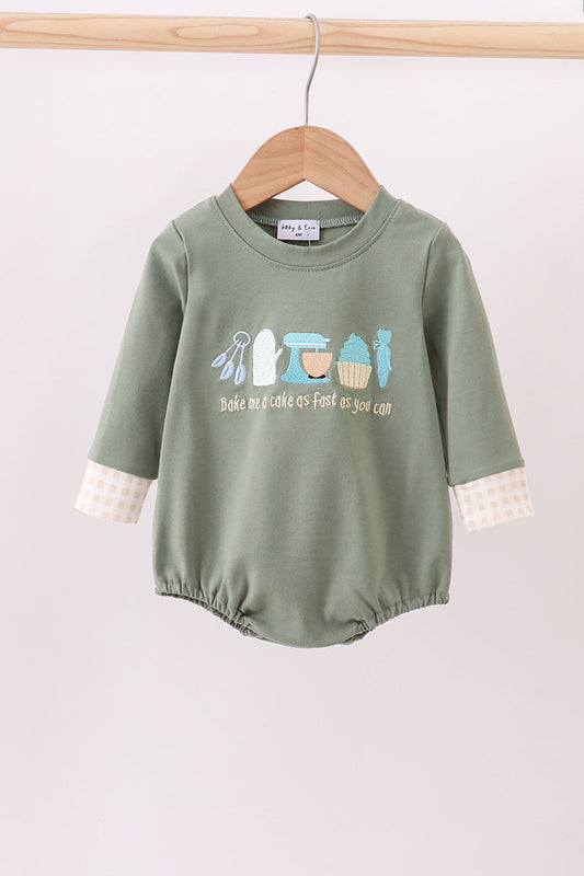 Green baby romper with printed design on a wooden hanger against a light background