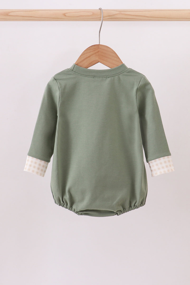 Green baby romper with white cuffs on a wooden hanger against a light background