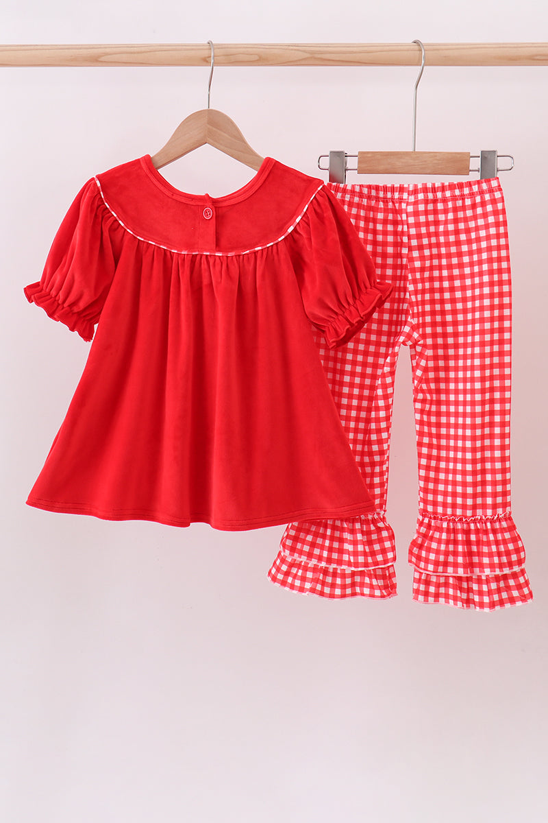 Red dress with ruffled sleeves and checkered pants on a hanger against a light background