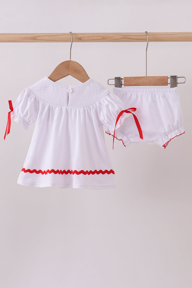 White top and shorts set with red trim on a wooden hanger against a white background