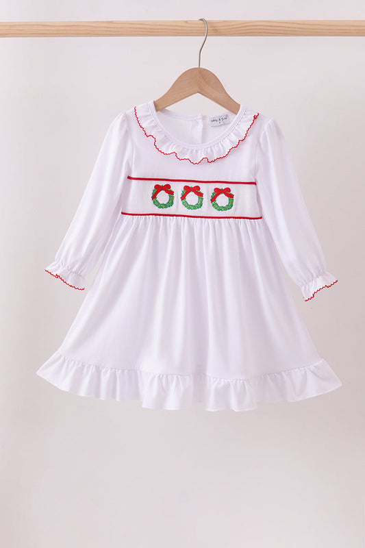 White dress with red trim and green floral patterns on a hanger against a beige background