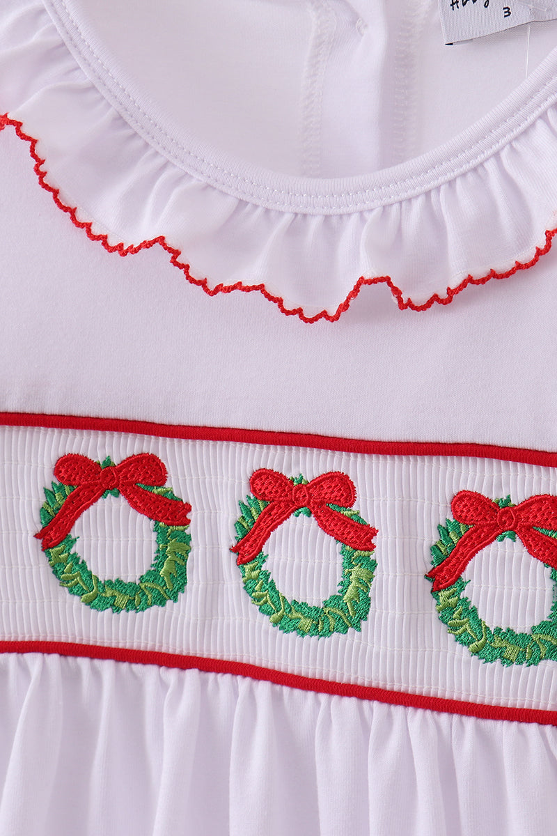 White dress with red and green embroidery of wreaths and bows on a white background.