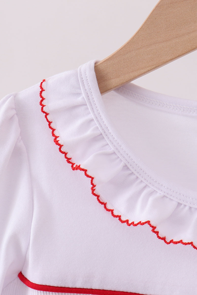 White garment with red trim on a wooden hanger against a white background