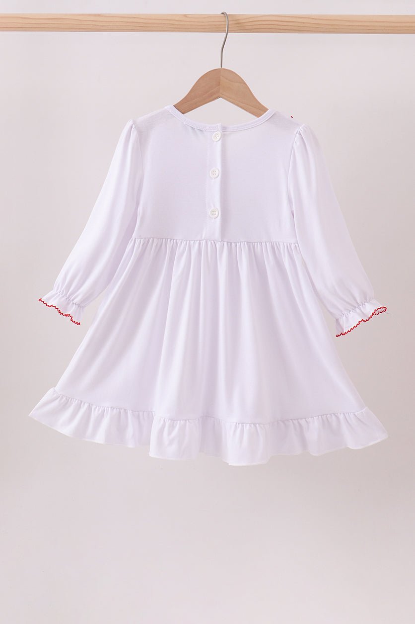 White dress with red trim on a wooden hanger against a beige background