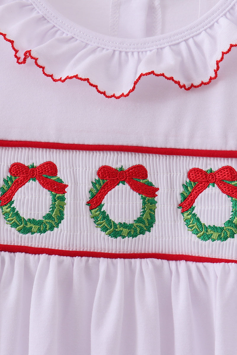 White dress with red trim and embroidered Christmas wreaths and bows on a white background