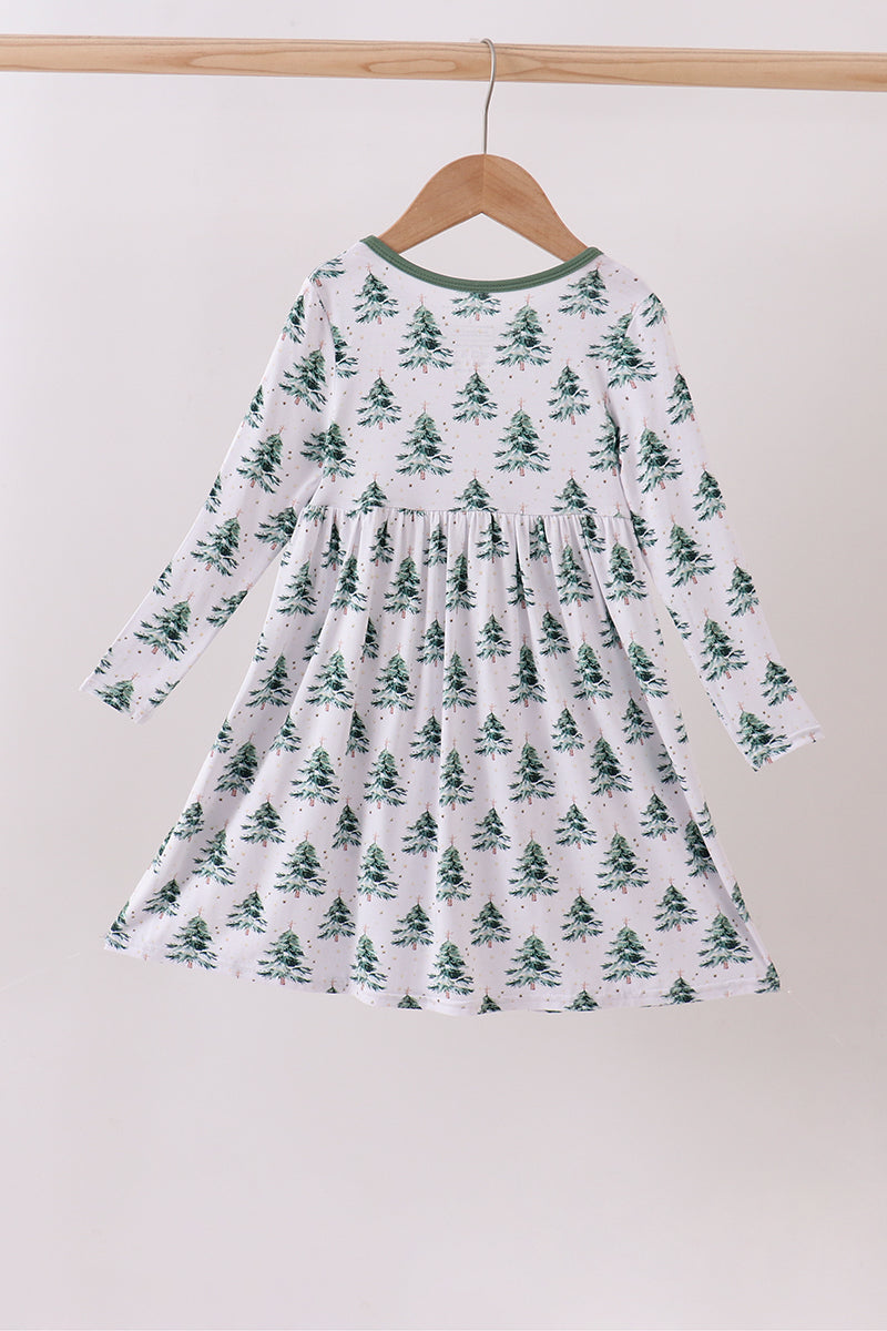 White dress with green tree pattern hanging on a wooden hanger against a white background