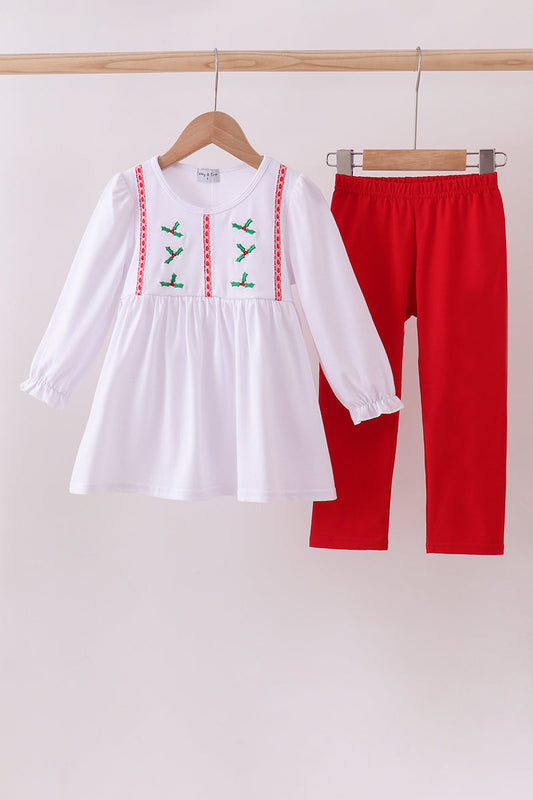 White blouse with green embroidery and red pants hanging on a rack against a white background