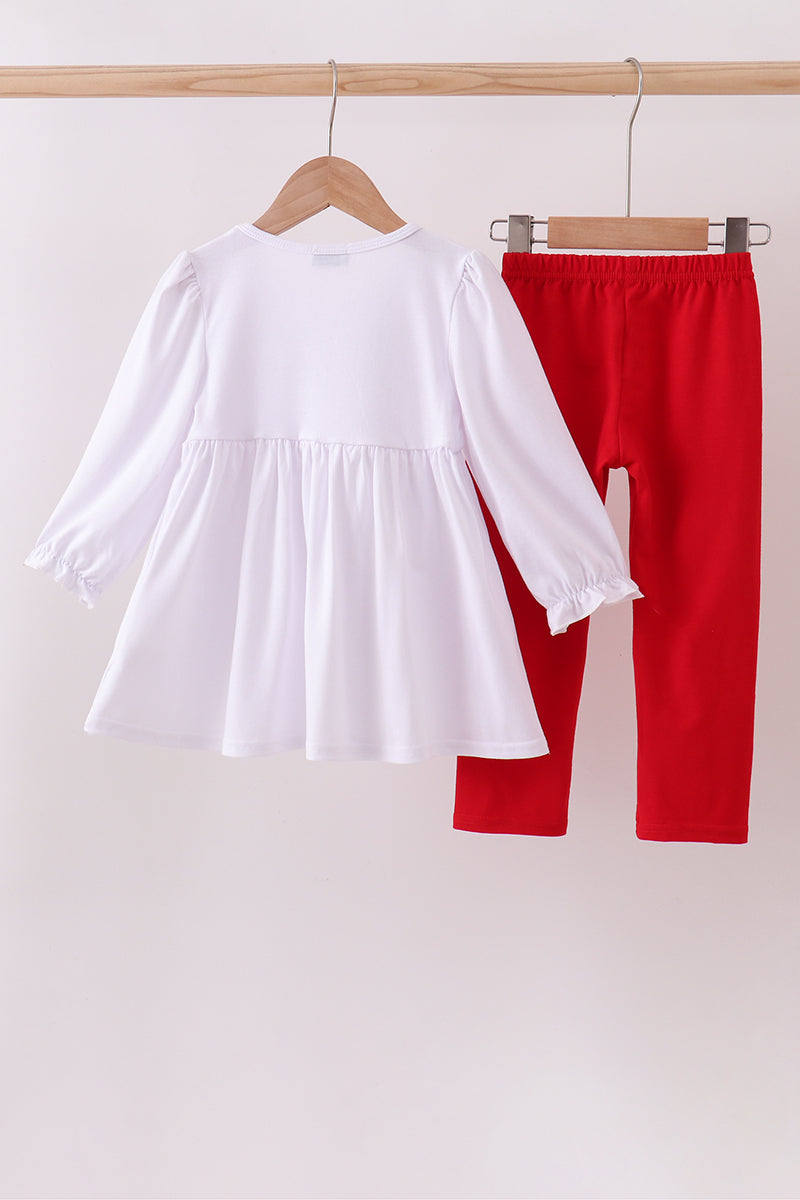 White blouse and red pants hanging on a wooden rack against a white background