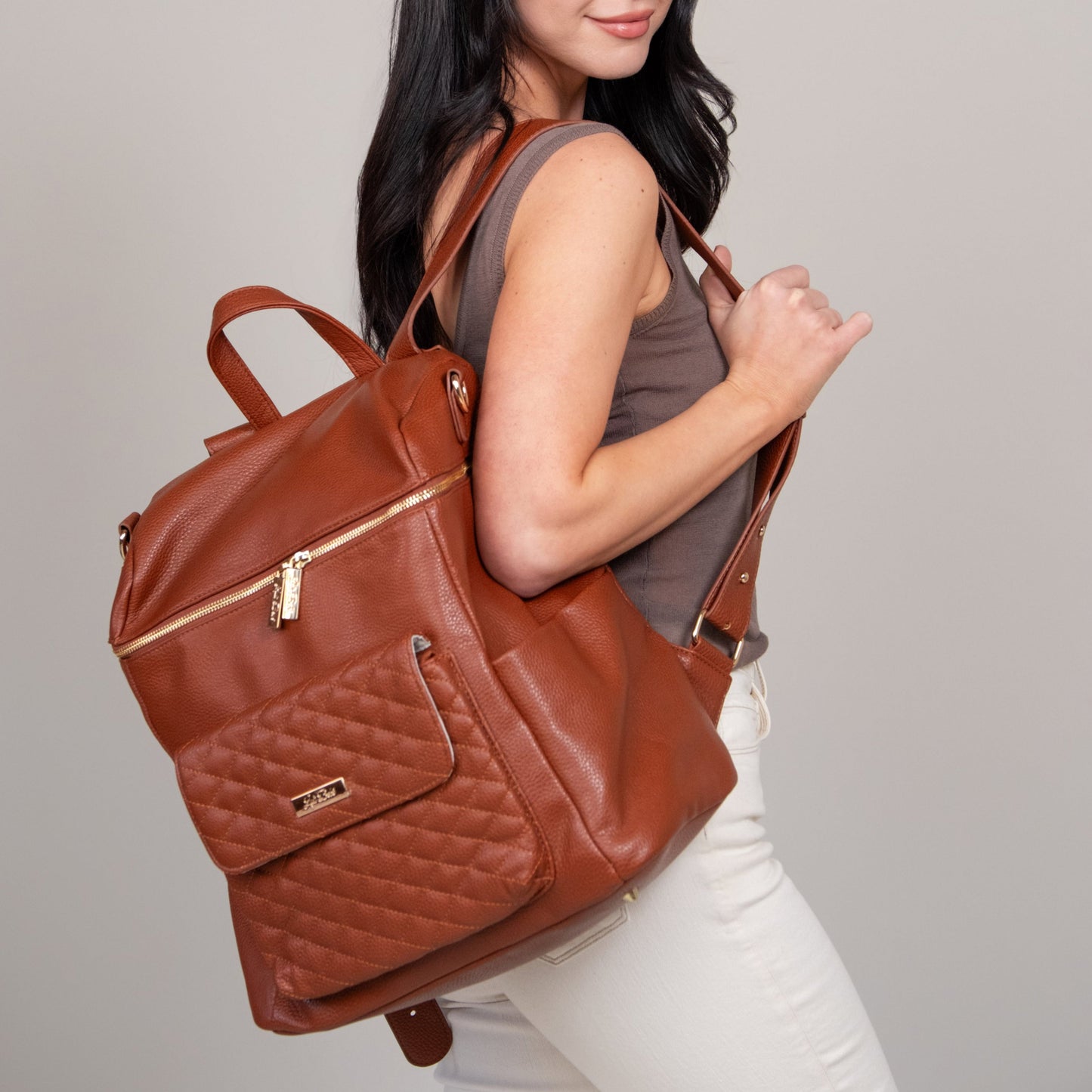 Woman carrying a brown leather backpack against a plain background