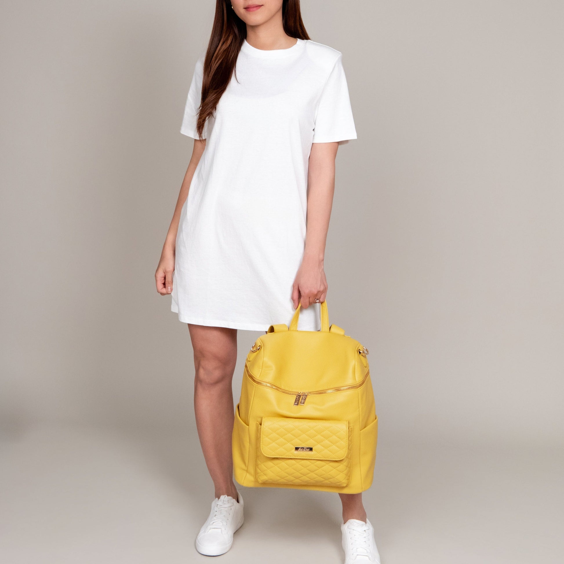 Person holding a yellow backpack against a neutral background