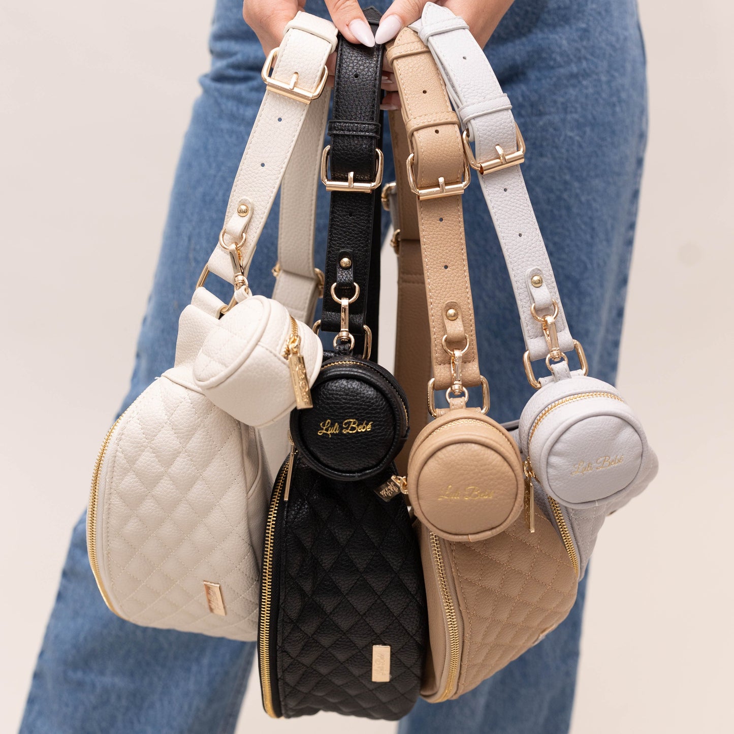 Four handbags with different colors and designs held by a person wearing blue jeans.