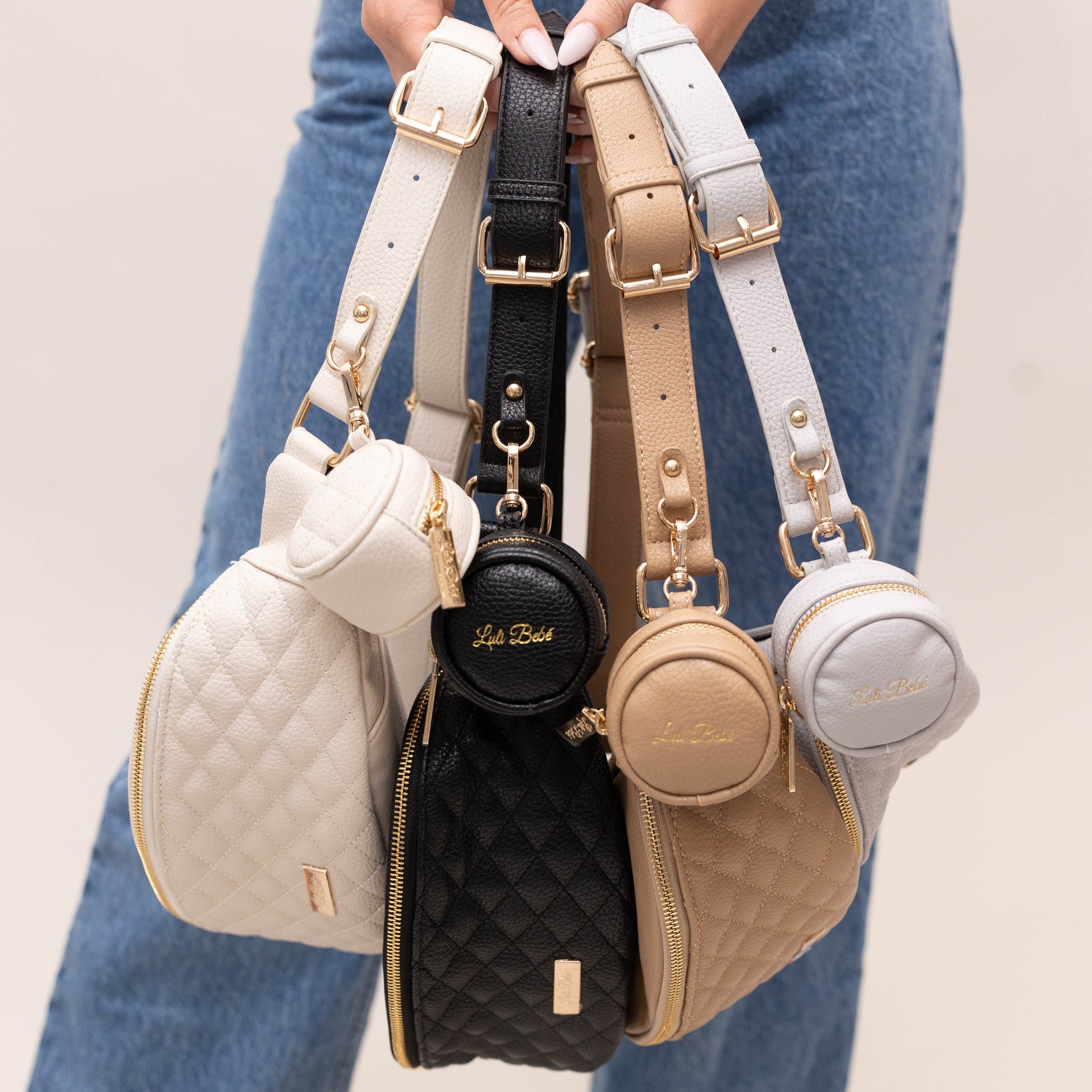 Four handbags with different colors and designs held by a person wearing blue jeans.