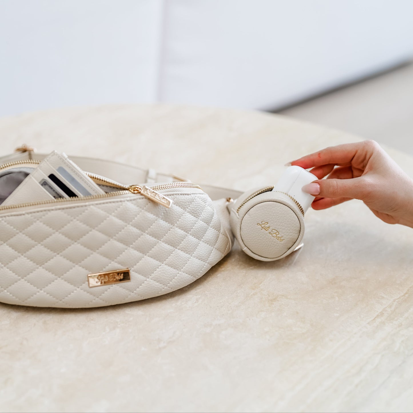 White quilted bag with a hand holding a white earbud case on a light surface.