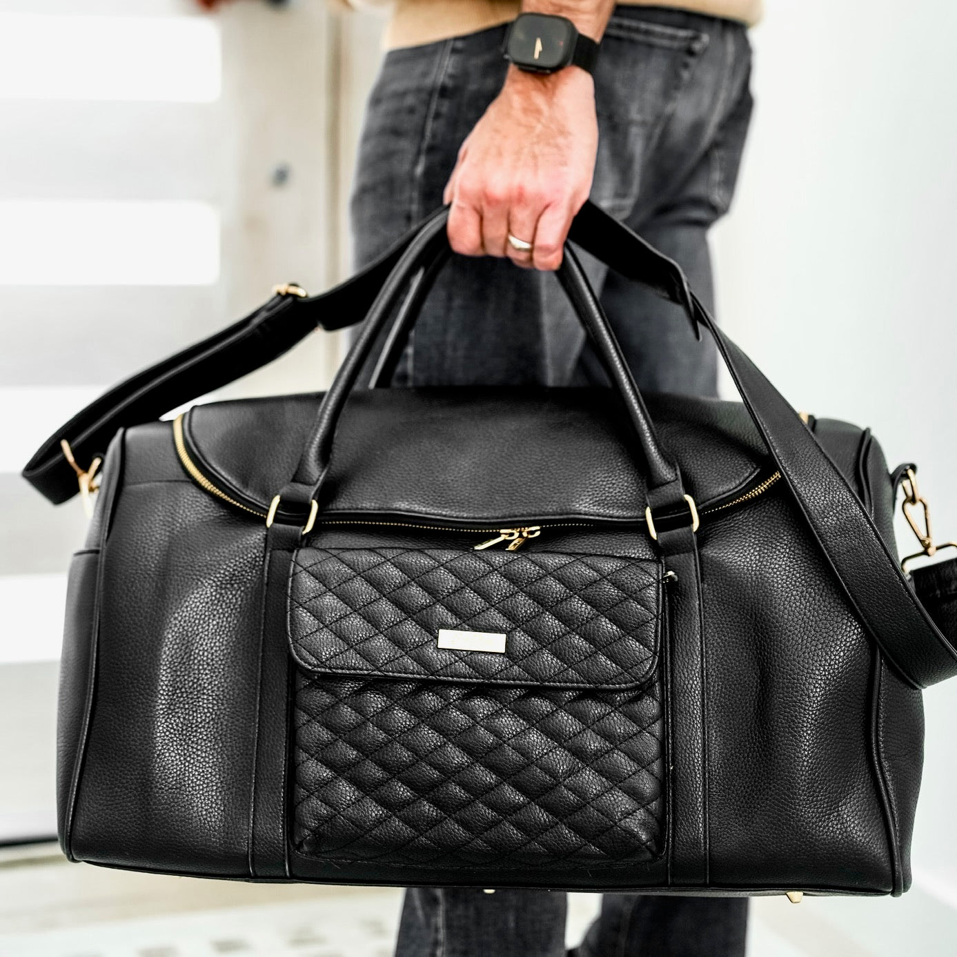 Black quilted duffel bag held by a person with a neutral background