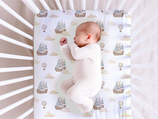 Baby lying on a crib mattress with a ship patterned sheet