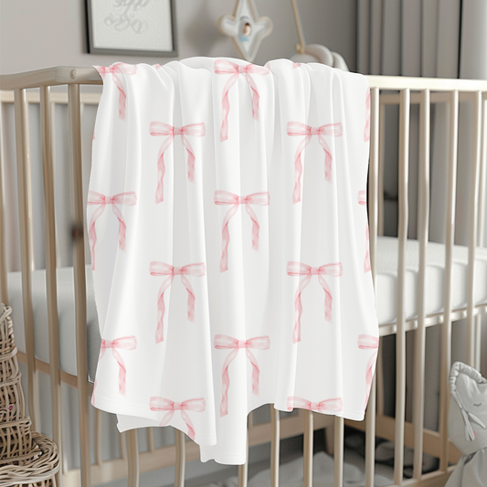 White crib with a pink bow patterned blanket in a nursery setting.