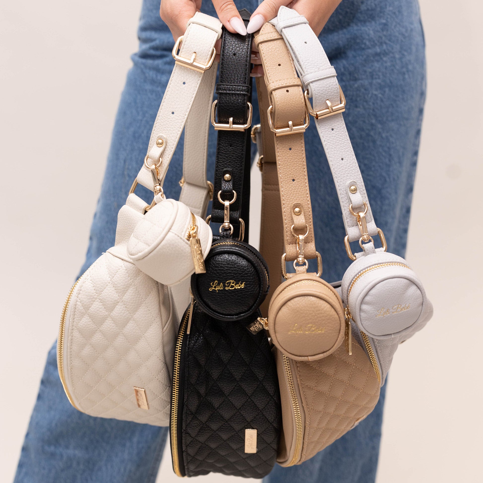Set of four small handbags in different colors held by a person wearing blue jeans.