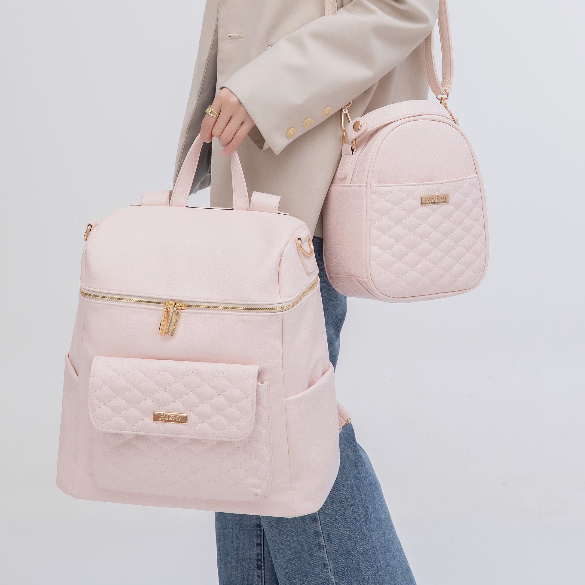 Person holding two pink bags, one backpack and one quilted bag, on a light gray background.