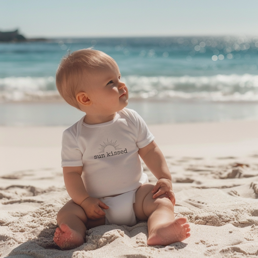 Baby sitting on a sandy beach wearing a 'sun kissed' onesie.