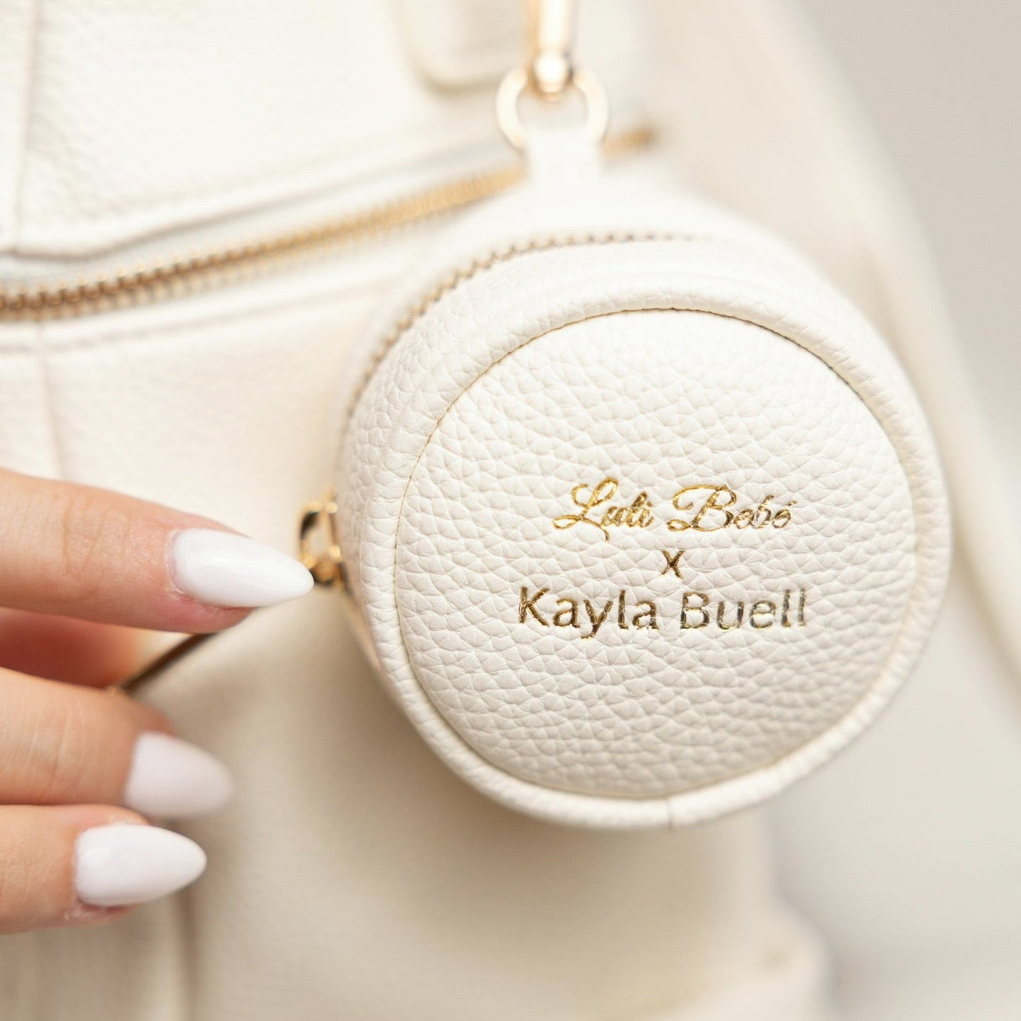 Round white case with 'Lulu Bube' and 'Kayla Buell' branding held by a hand.