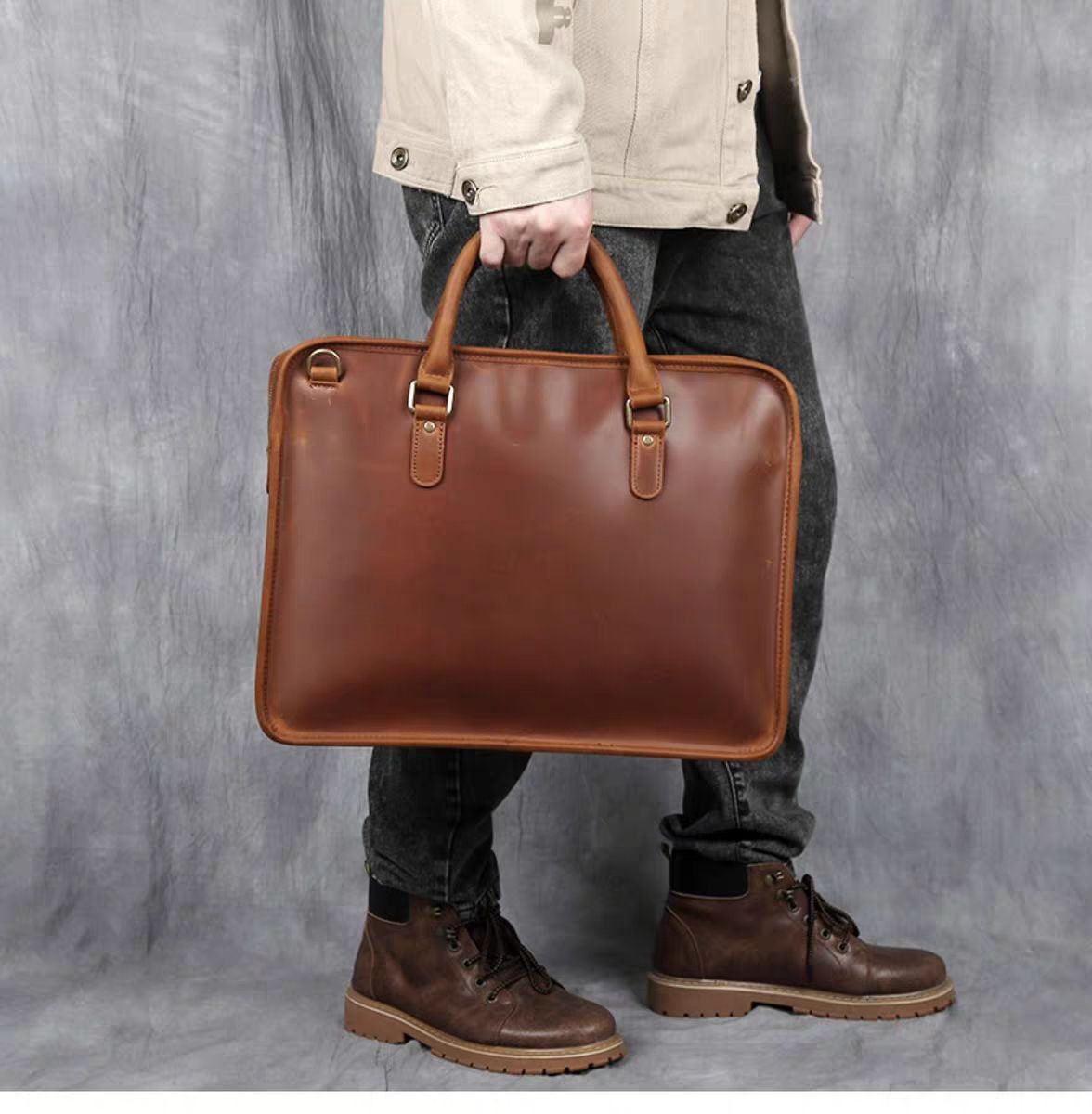 Person holding a brown leather briefcase against a gray background