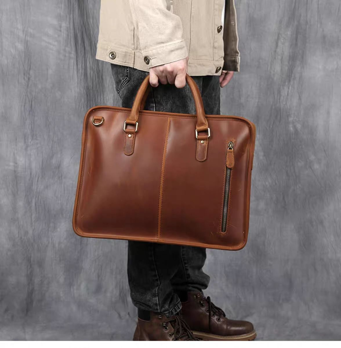 Person holding a brown leather briefcase against a gray background