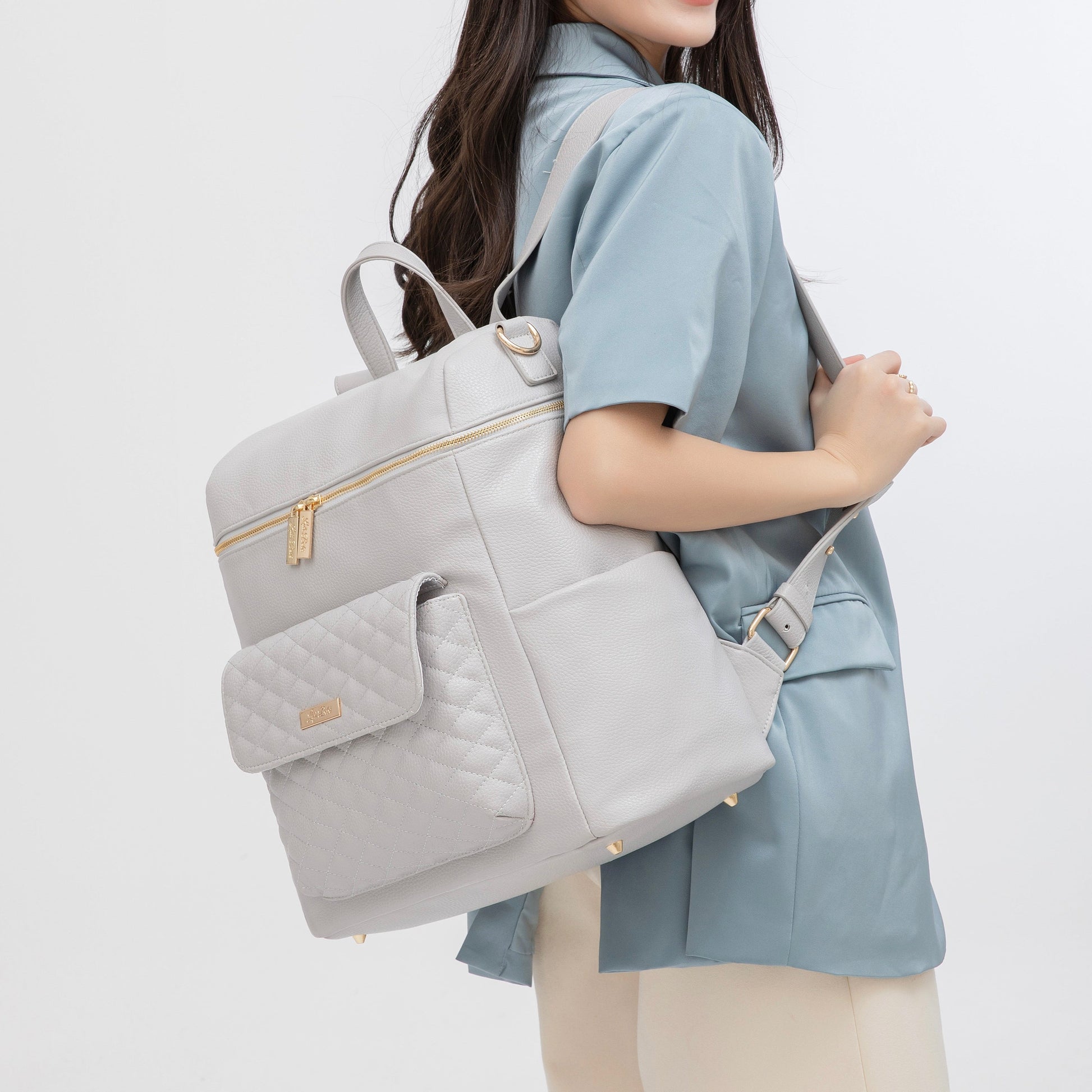 Person holding a light gray backpack with gold zippers on a white background