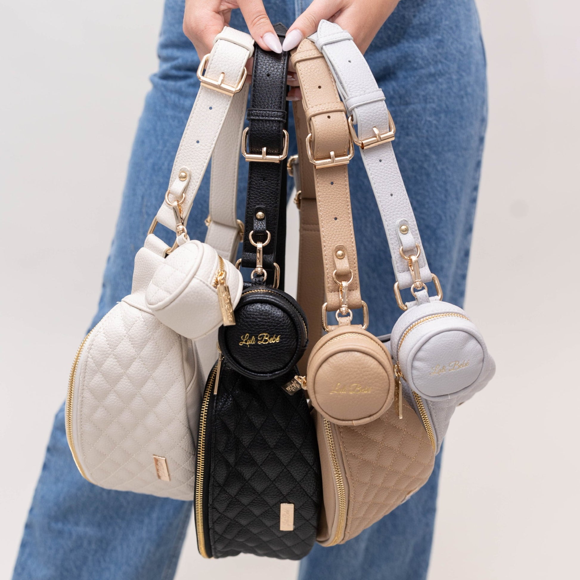 Five small handbags with matching straps held by a person wearing blue jeans.