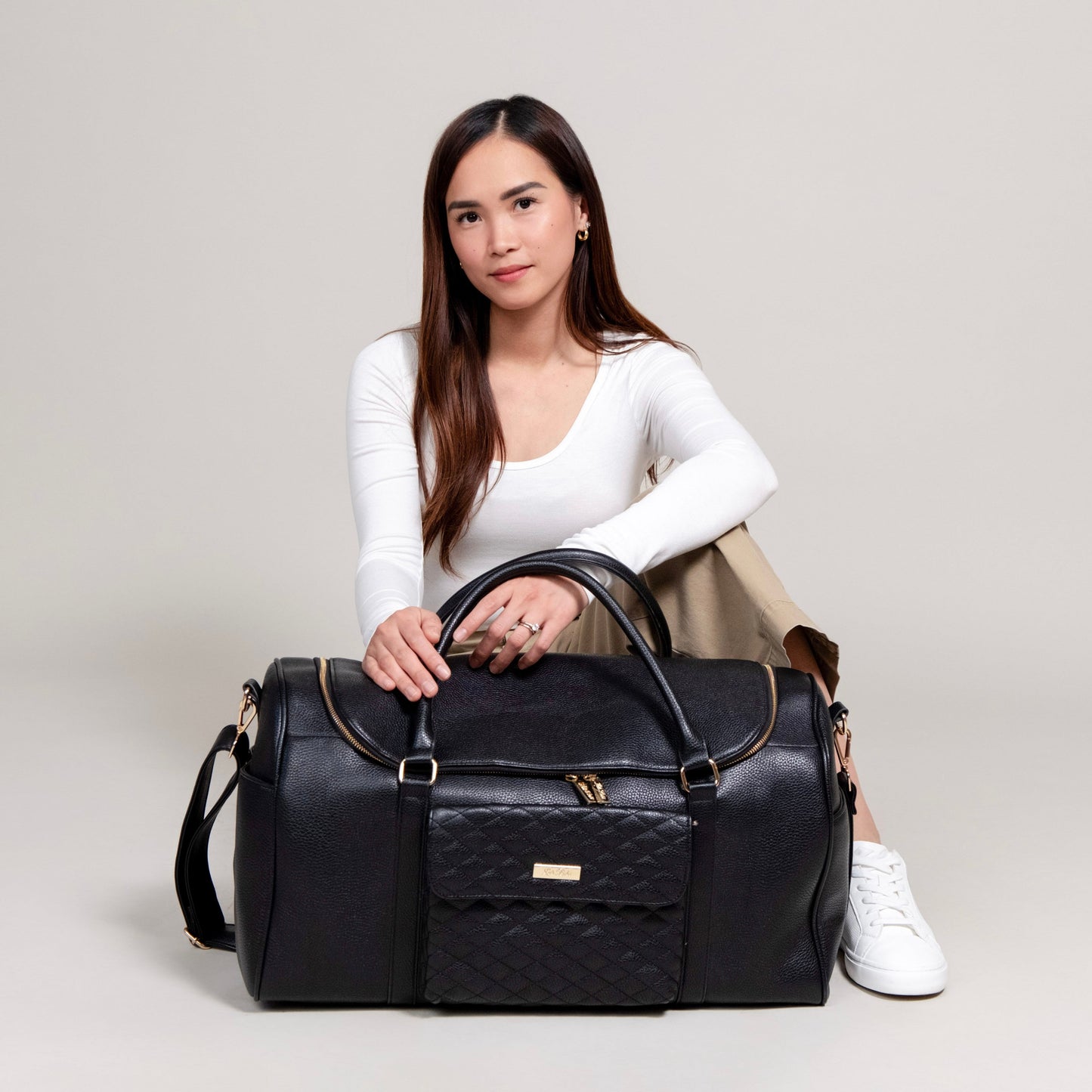 Woman holding a black quilted duffel bag against a plain background