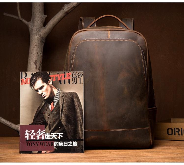 Brown leather backpack on a wooden surface with a magazine featuring a man in a suit.