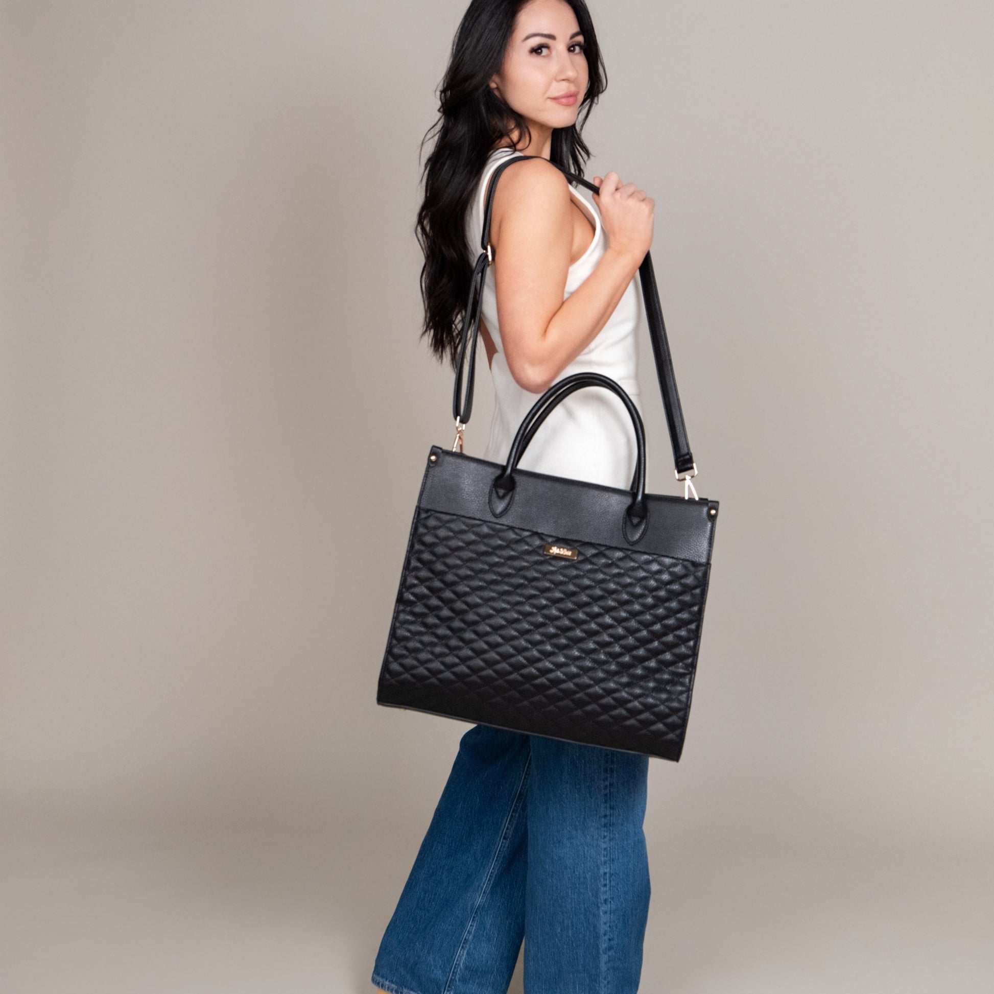 Woman holding a black quilted handbag against a neutral background