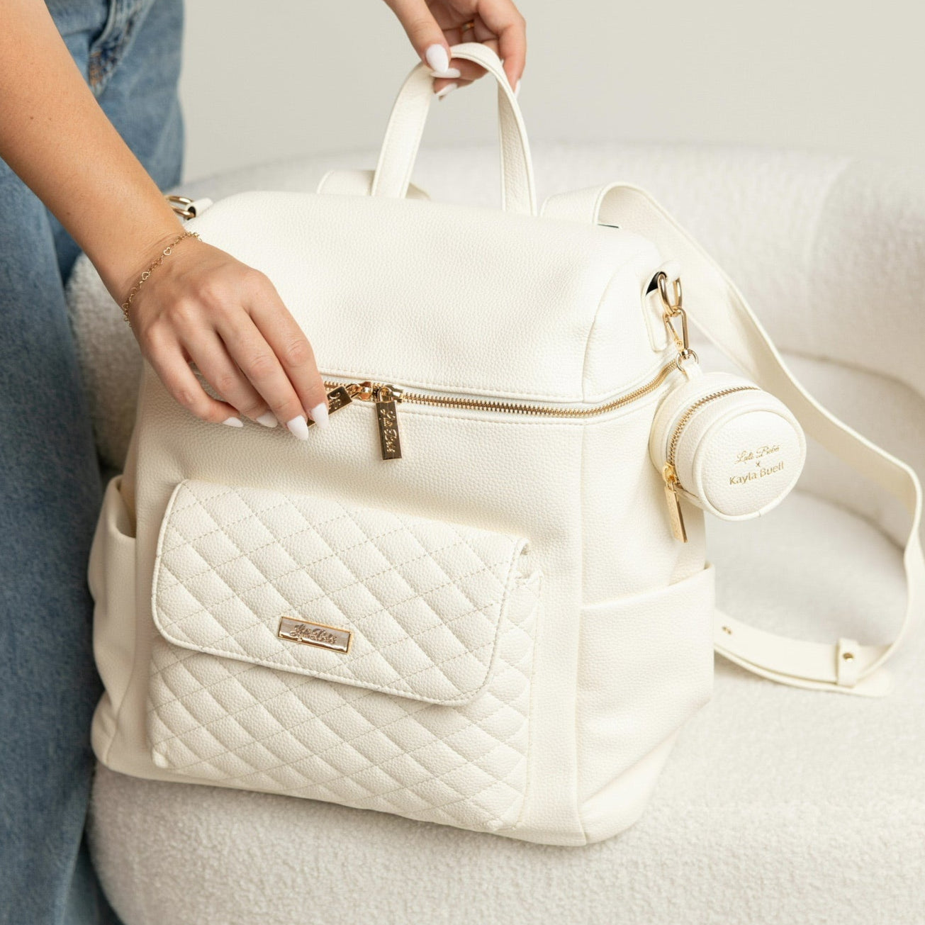 White quilted backpack with gold accents held by a person on a light background