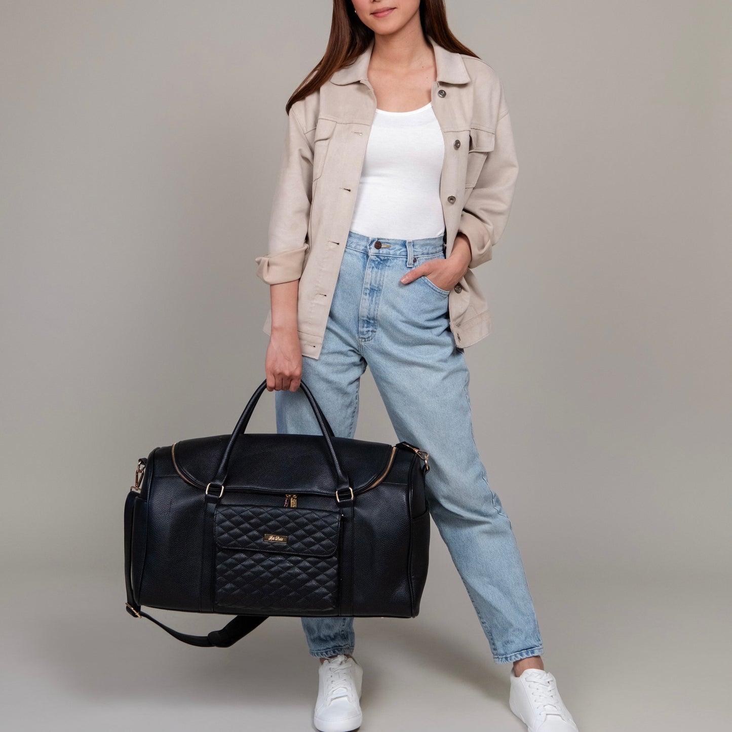 Person holding a black quilted duffel bag against a neutral background